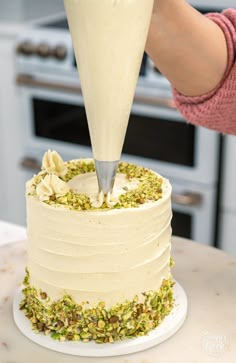 someone is pouring frosting onto a cake with pistachios on the top