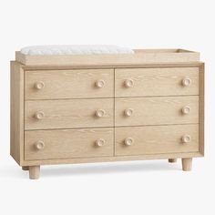 a baby crib with white mattress and wooden drawers