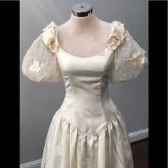 a white dress on a mannequin with laces and flowers in the sleeves