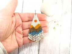 a hand holding a beaded earrings on top of a wooden table