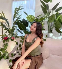 a woman sitting on top of a white couch next to potted plants and greenery