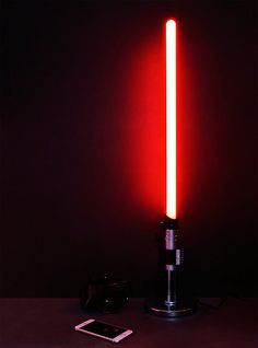 a red light saber sitting on top of a table next to a cell phone and remote control