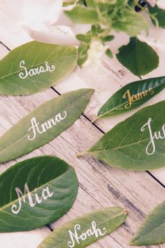 some leaves with names on them sitting on a wooden table next to flowers and greenery