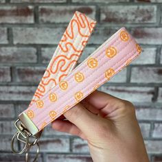 a hand holding a keychain with an orange and white pattern on it, in front of a brick wall