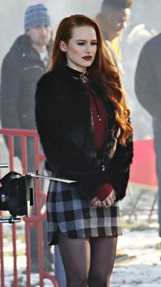 a woman with long red hair wearing a black and white checkered skirt while standing in front of a camera