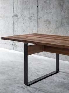 a wooden table with metal legs in front of a concrete wall and cement flooring