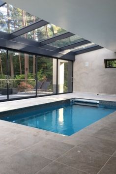 an indoor swimming pool surrounded by glass walls and windows with sliding doors leading to the outside