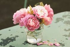 pink flowers are in a glass vase on an old table with petals scattered around it