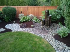 a garden area with rocks, plants and water features in the center is a wooden fence