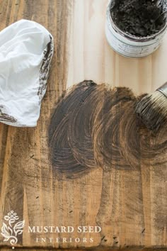 a wooden cutting board with some paint and a brush on it next to a container of dirt