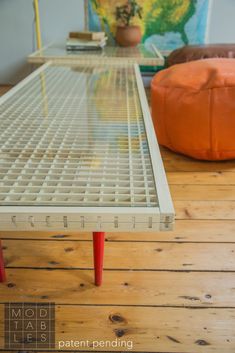 an orange ottoman sitting on top of a wooden floor next to a white table with red legs