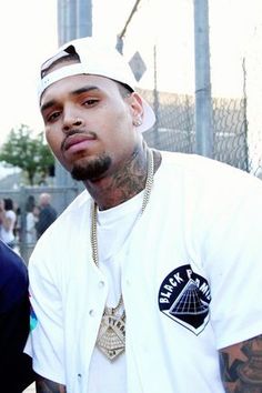 two men standing next to each other in front of a chain link fence with people behind them