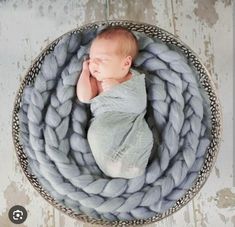 a newborn baby wrapped in a blanket is laying on top of a round basket with his hands under his chin