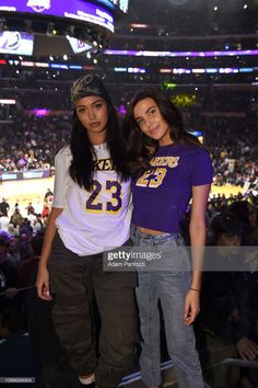 two young women standing next to each other in front of a crowd at a basketball game