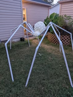 a white spider sculpture sitting in the grass next to a house with a flower on it's back end