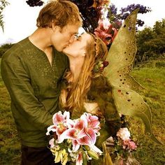 a man and woman kissing in the grass with flowers on their heads, dressed as tinkerbells