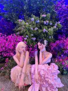 two young women sitting on the ground in front of some purple and pink flowers with their hands to their face