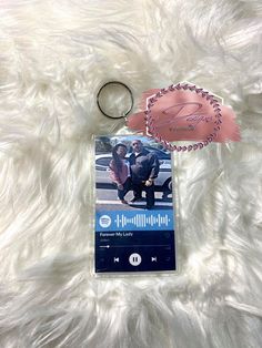 an mp3 player keychain is laying on top of a white furry surface with a pink ribbon around it