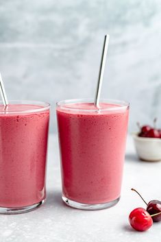 two glasses filled with smoothie next to a bowl of cherries