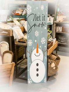 a wooden sign that says, let it snow with a snowman on it and some baskets in the background