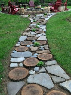 a stone path made out of logs in the middle of a grassy area with chairs around it