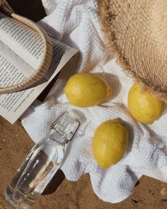 three lemons on a towel next to a bottle of water and a straw hat