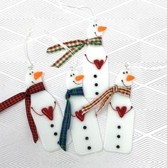 four snowmen wearing scarves and scarfs are hanging from strings on a white surface