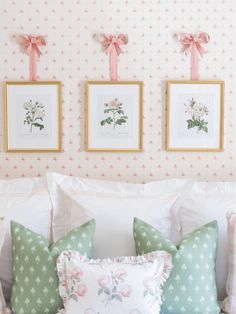 two framed pictures hang on the wall above a bed with white sheets and pink bows