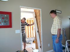 two men standing in a living room next to each other looking at something on the wall