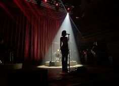 a woman standing in front of a microphone on top of a stage next to a red curtain