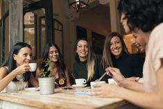 four women sitting at a table drinking coffee and laughing with each other in front of them