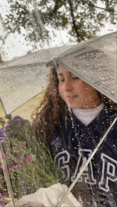 a girl holding an umbrella in the rain with purple flowers behind her and water splashing on her face