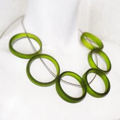 a green necklace is sitting on a white cloth with four rings hanging from it's center