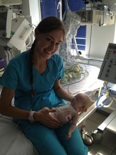 a woman in scrubs holding a baby in a hospital bed with medical equipment around her