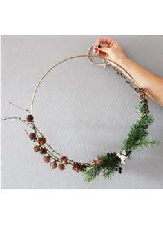 a person is holding a wreath with pine cones and other decorations on the inside of it