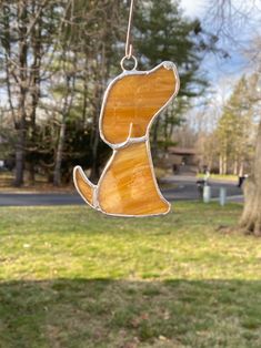 a stained glass dog ornament hanging from a string in a park with trees