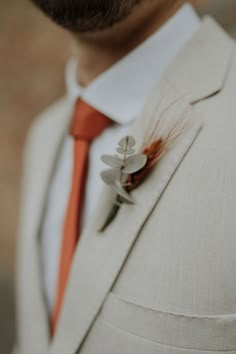 a man in a suit and tie with an orange flower on his lapel pin