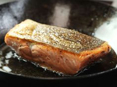 a piece of salmon being cooked in a frying pan with oil on it's side