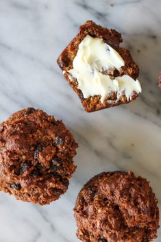 three chocolate muffins with cream on top and one in the middle, sitting on a marble surface