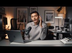 a man sitting in front of a laptop computer talking on the phone and holding his hand up to his ear