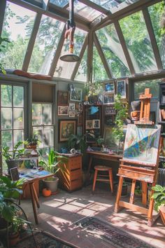 an artist's studio with lots of plants in the window sill and paintings on the wall