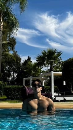 a man sitting in the middle of a swimming pool with sunglasses on his face and palm trees behind him