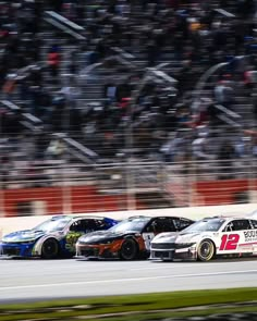 three race cars driving around a track in front of a crowd