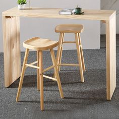 two stools and a table with a plant on it in front of a white wall