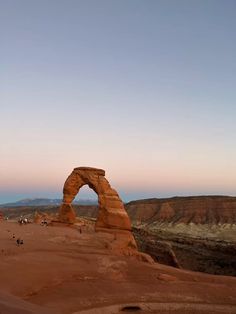 an arch shaped rock formation in the middle of desert with people walking around it at sunset