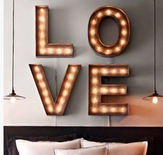 the word love is lit up with light bulbs in front of a bed and pillows