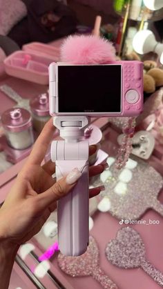 a person holding up a pink camera in front of a table filled with other items