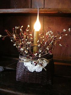 a candle is lit in a basket with branches and berries on the table next to it