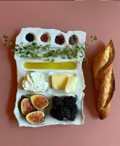 an assortment of cheeses, fruits and bread on a pink plate next to a baguette