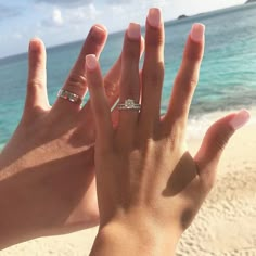 two hands with wedding rings on their fingers at the beach and water in the background